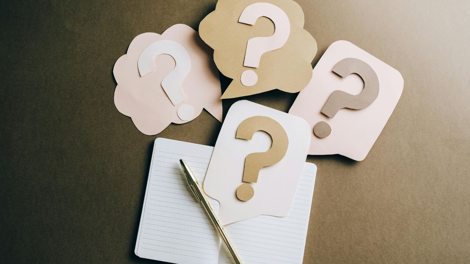 Paper question marks arranged next to an open notebook and pen