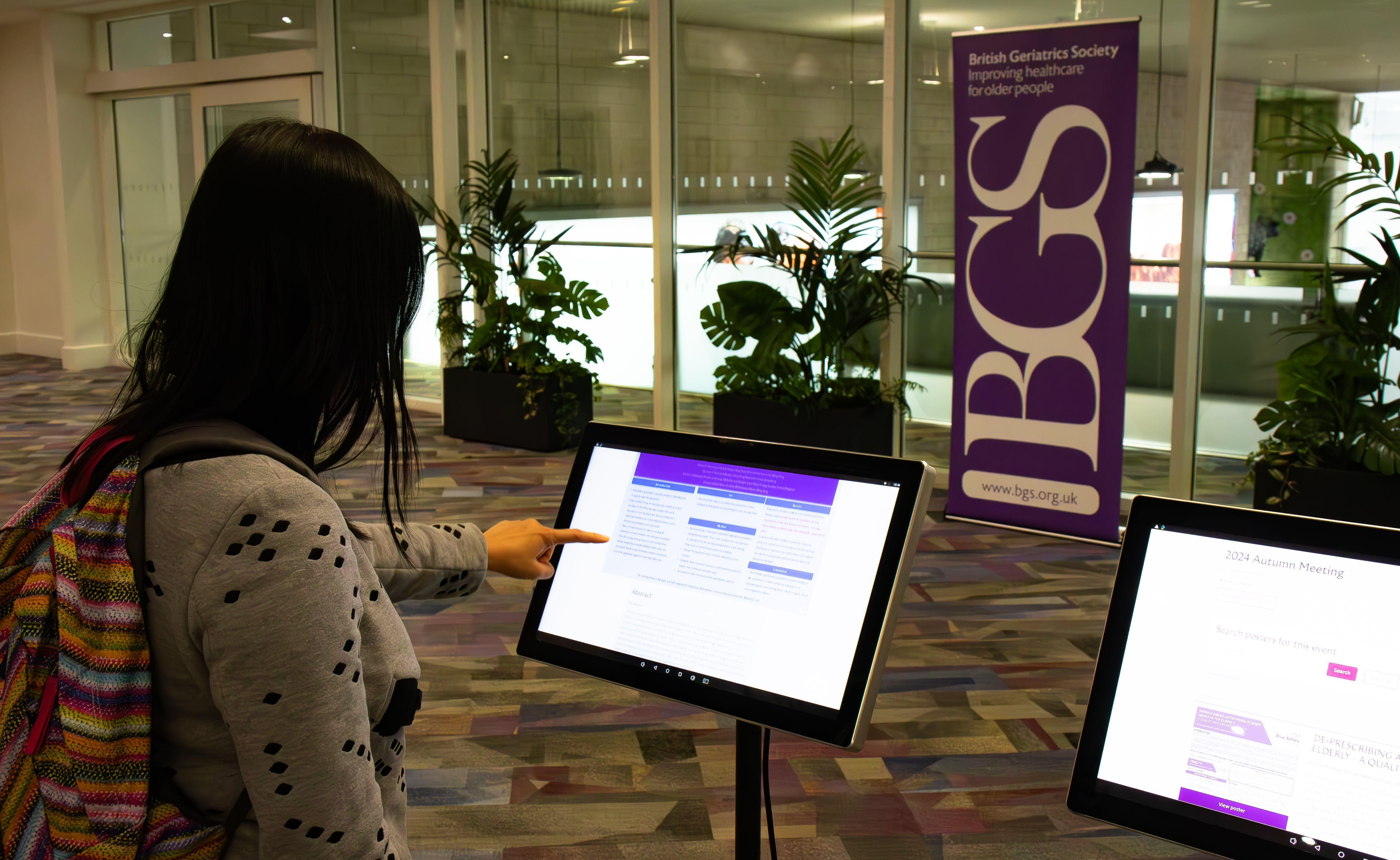 Woman looking at a BGS poster screen at a conference with the BGS sign in the background