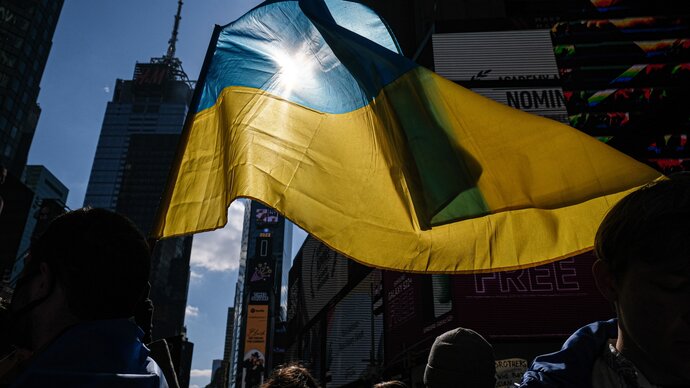Ukrainian flag with sun shining through it with skyscrapers behind it